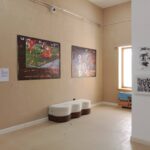The Techspressionism show in a gallery room in Khiva, Uzbekistan with abstract posters on the wall, a white and brown bench, and artwork displayed on a pillar.