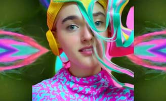 A person wearing a colorful, abstract outfit with bright patterns and a yellow headpiece, surrounded by swirling, multicolored digital effects and vibrant, psychedelic background designs.