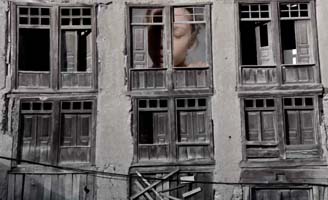 A weathered building with broken and missing window panes. In one upper window, a large image of a childs face is visible, eyes closed, partially obscured by shadow.
